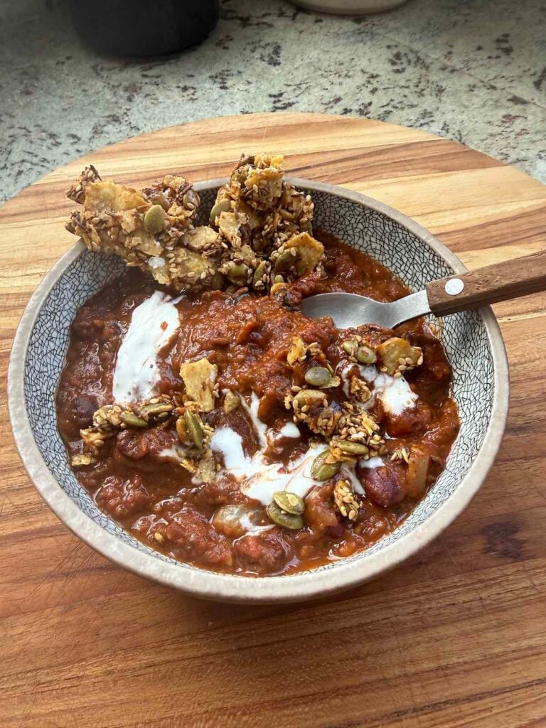 bowl of charred vegetable chili topped with crema, with spoon and tortilla crisps.