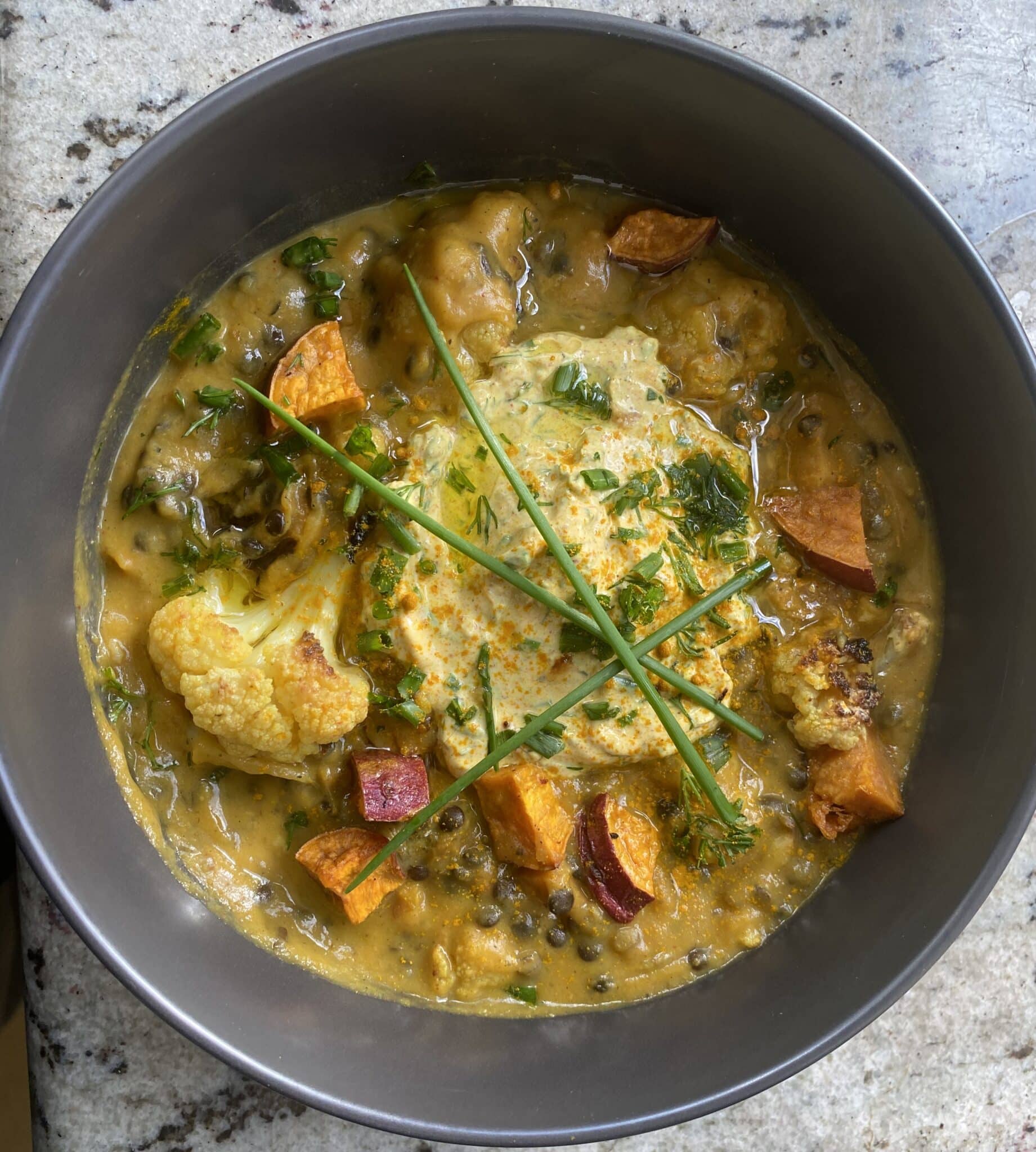 overhead view of a bowl of roasted sweet potato and cauliflower soup with toppings