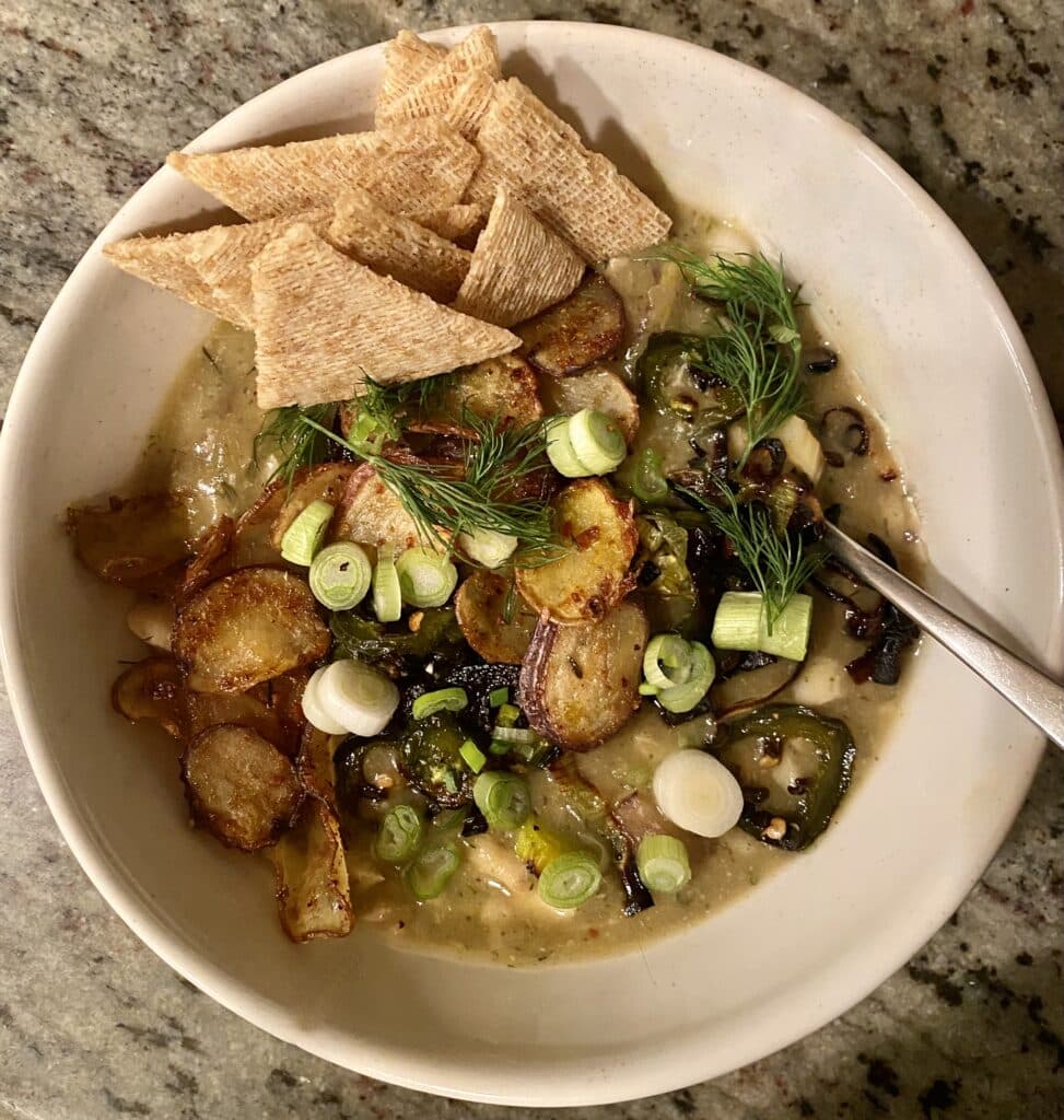 fish and potato stew in bowl with spoon, served with toppings and crackers.