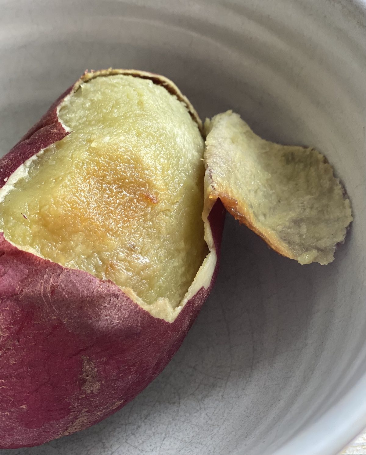 A cooked Japanese white sweet potato with its skin being peeled off.