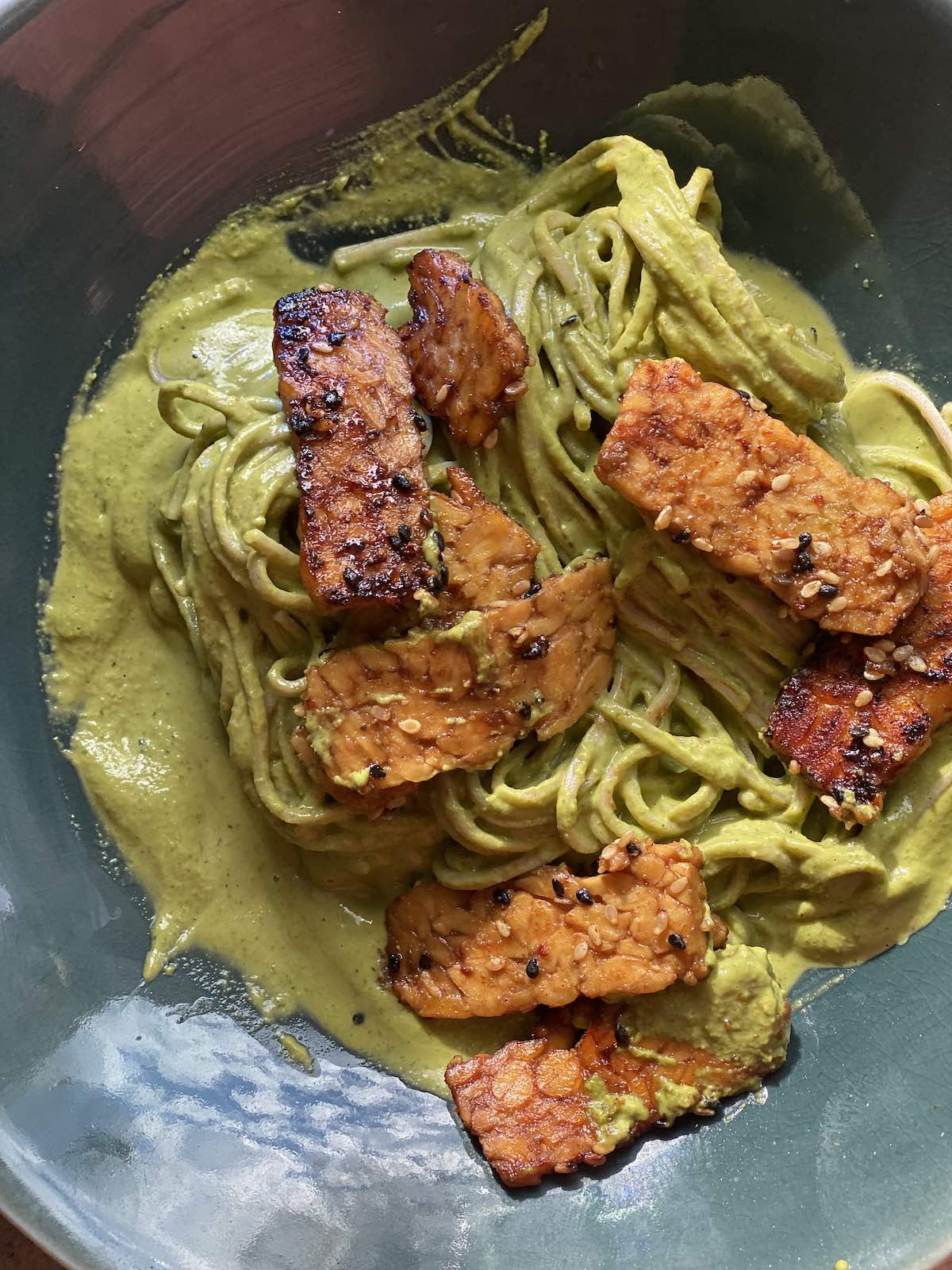 cooked tempeh slices are placed on top of tahini noodles.