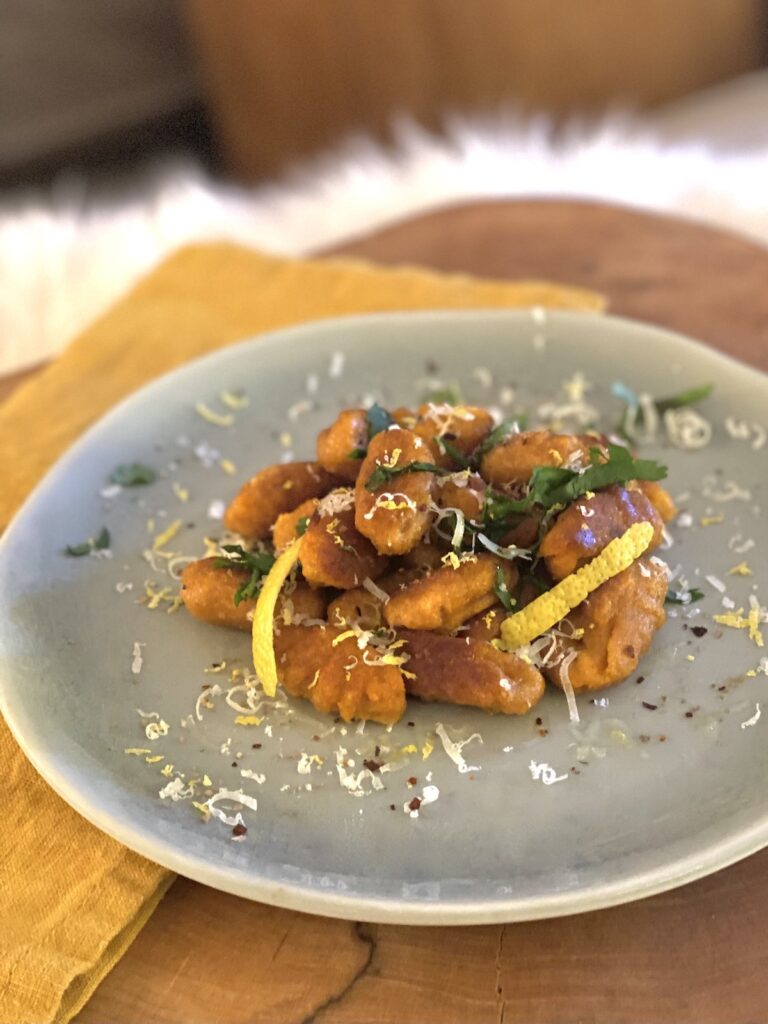 pan-seared orange sweet potato gnocchi plated with garnishes.