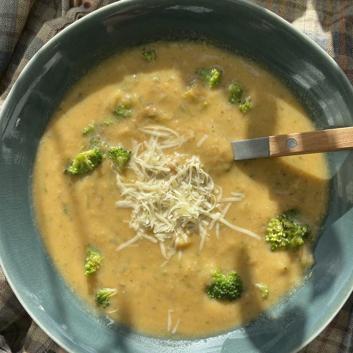 bowl of sweet potato and broccoli soup with spoon and grated cheese on top, shown from above.
