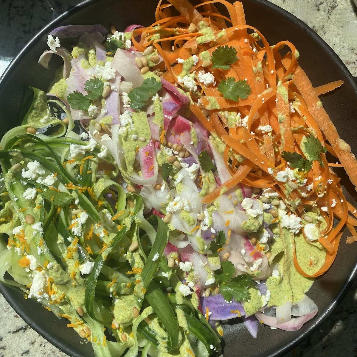 carrot, cucumber and daikon salad arranged by color on a serving platter with dressing and garnished with pine nuts and feta cheese.
