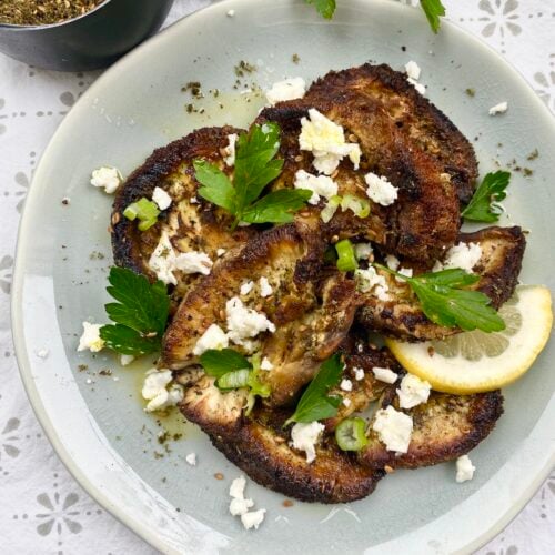 plate of sliced and sautéed lion's mane mushrooms garnished with parsley, lemon and feta.