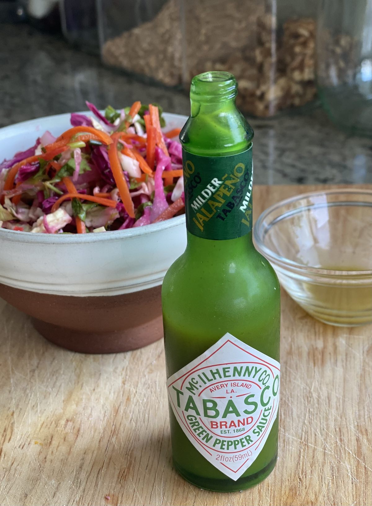 bottle of jalapeno tobasco sauce with bowl of slaw in background.