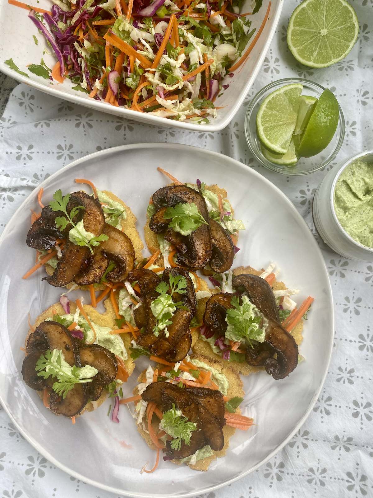 serving up mini tostadas with veggies, bowl of slaw and dish of avocado crema and lime wedges.
