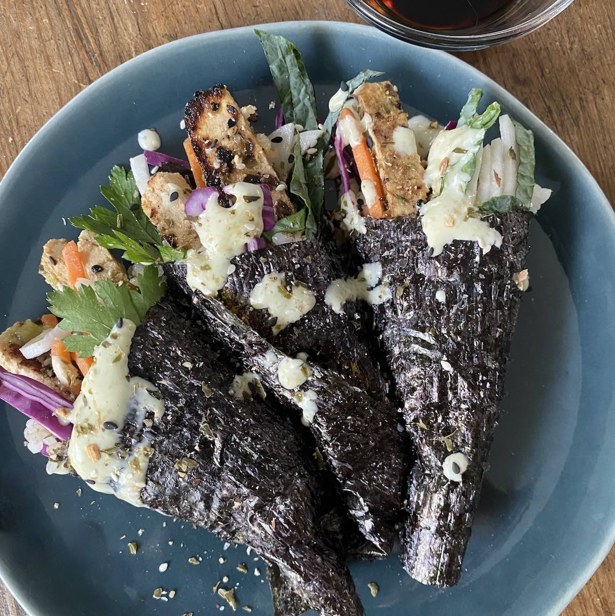 three tofu temaki sushi rolls, also known as hand rolls, on plate with side of tamari sauce.