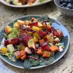 serving of stone fruit and veggie salad in front of larger serving platter of the salad and a bowl of blueberries.