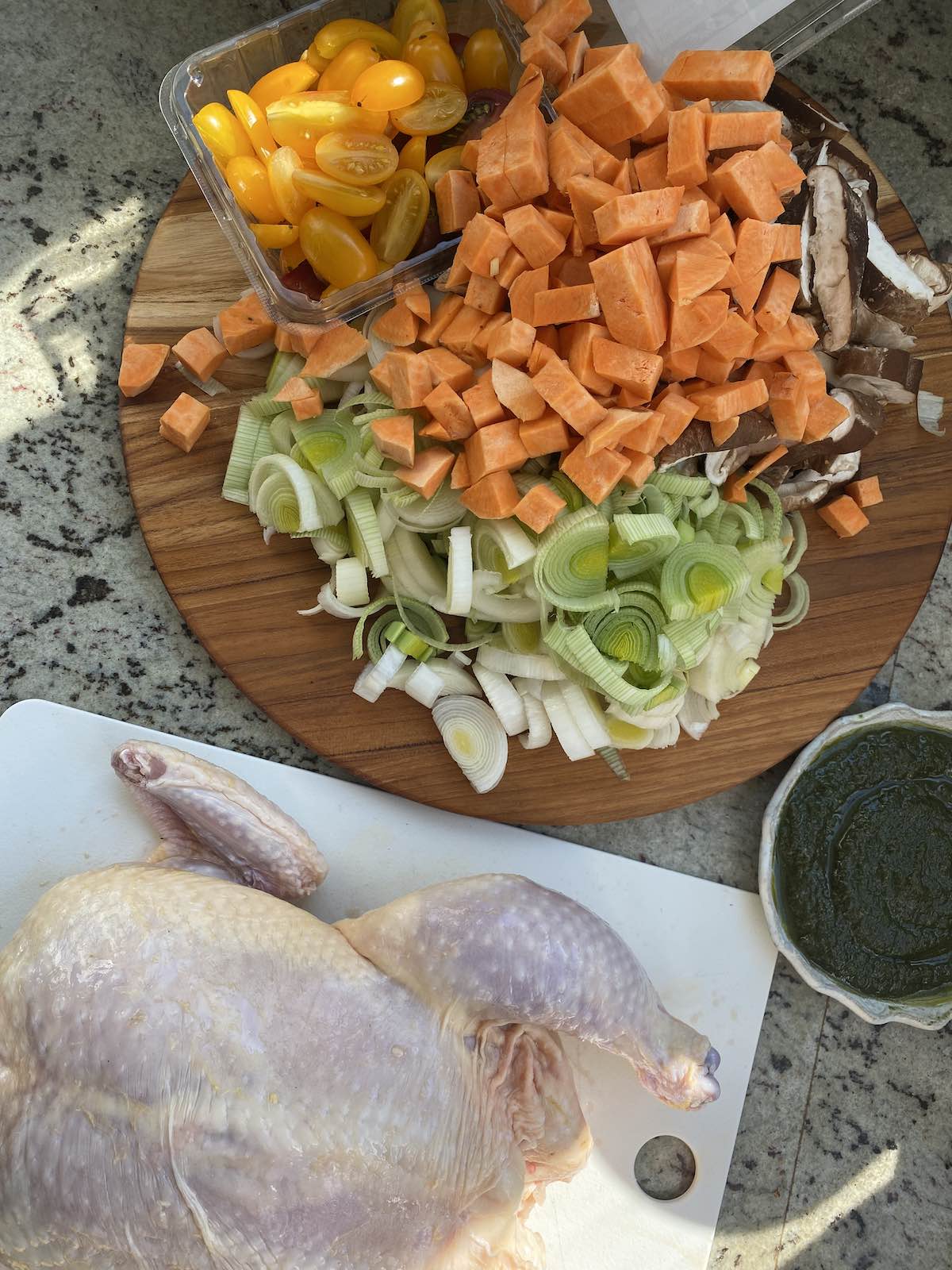 a whole raw chicken, homemade miso herb pesto and chopped vegetables ready for roasting are laid out next to each other, ready for preparation.