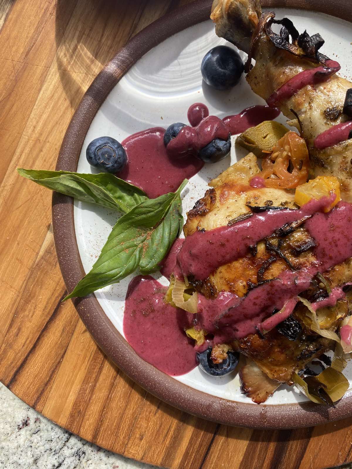 close up of roasted chicken leg with blueberry vinaigrette drizzled over the top and garnished with fresh basil leaves and blueberries.