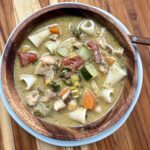top down view of hearty vegetable soup in wooden bowl on wooden cutting board.