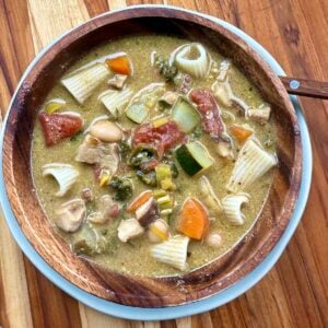 top down view of hearty vegetable soup in wooden bowl on wooden cutting board.