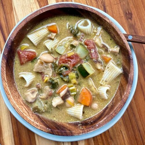 top down view of hearty vegetable soup in wooden bowl on wooden cutting board.