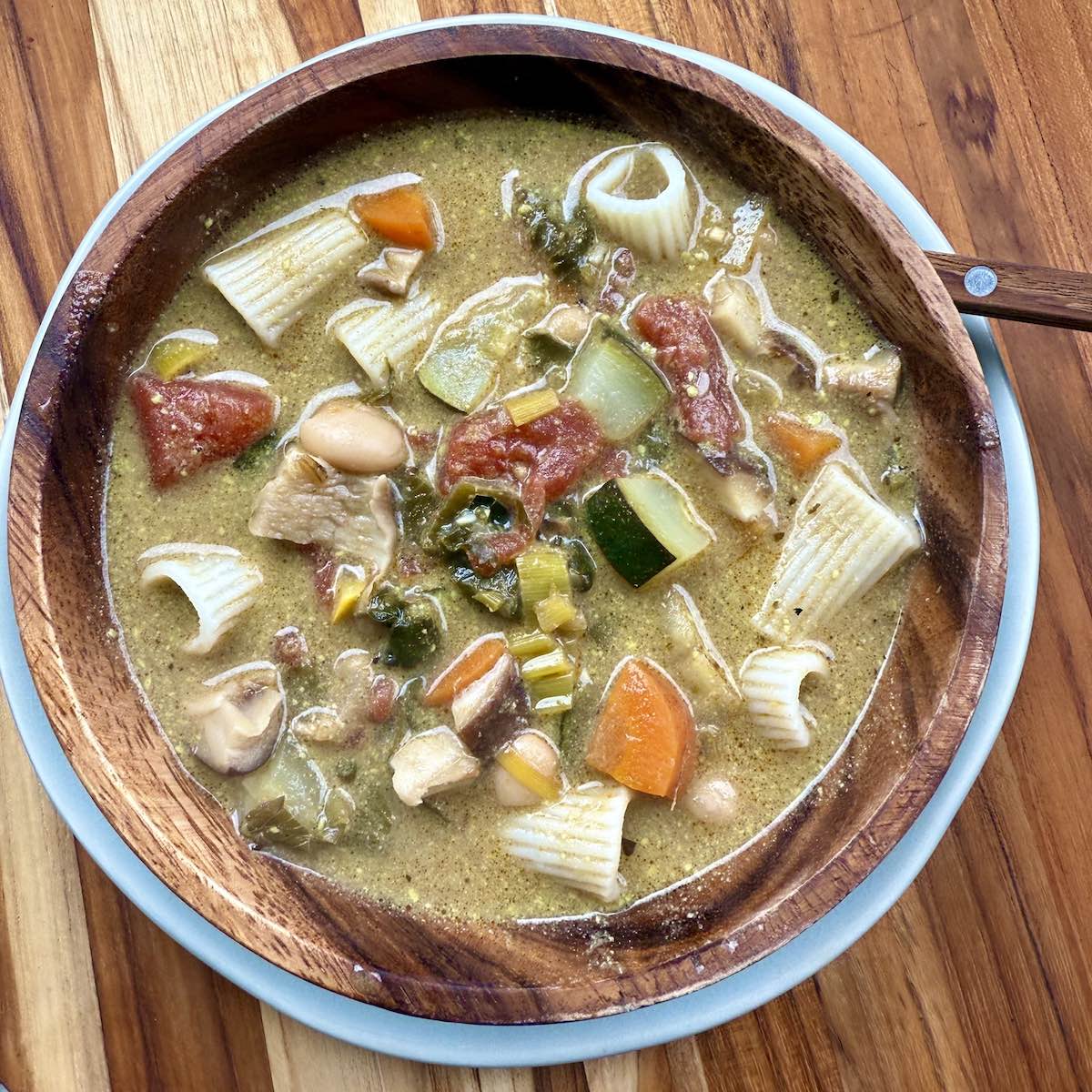 top down view of hearty vegetable soup in wooden bowl on wooden cutting board.