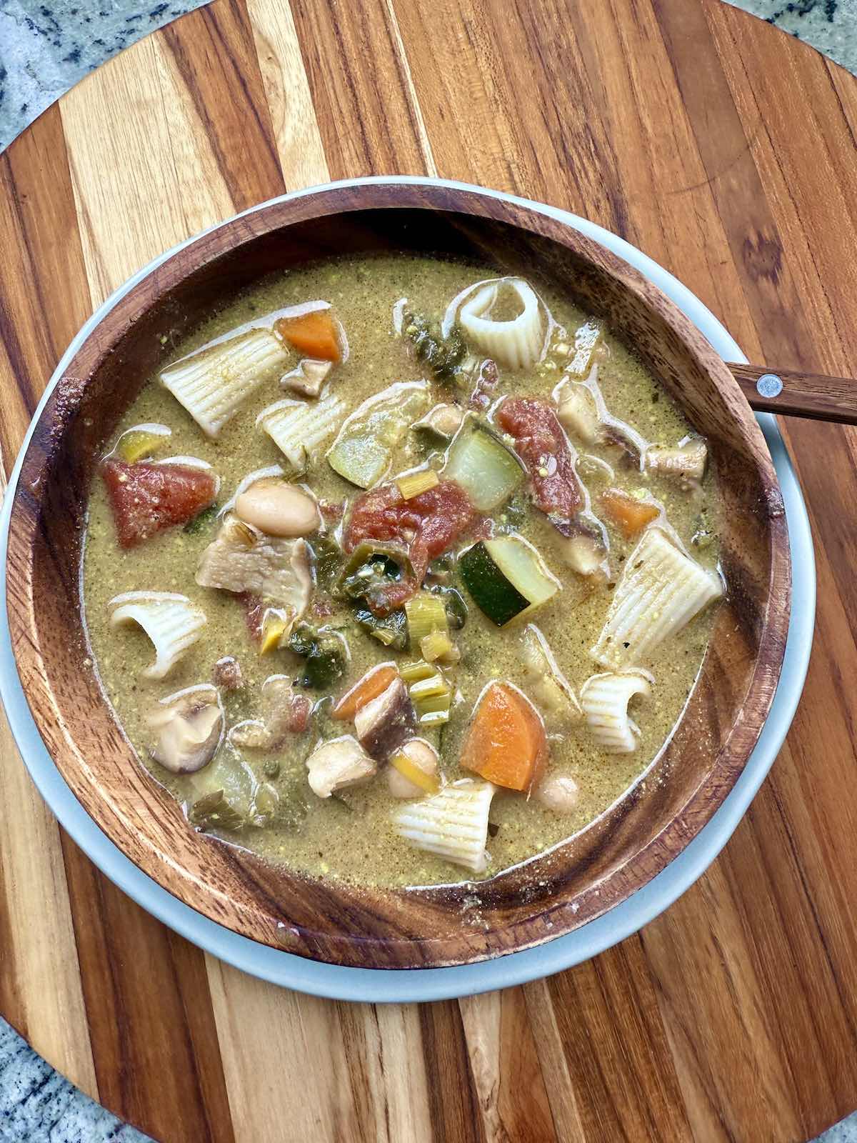top down view of hearty vegetable soup in wooden bowl on wooden cutting board.