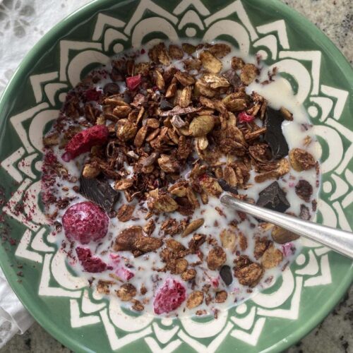 dark chocolate granola with dehydrated raspberries in a bowl with milk and a spoon.