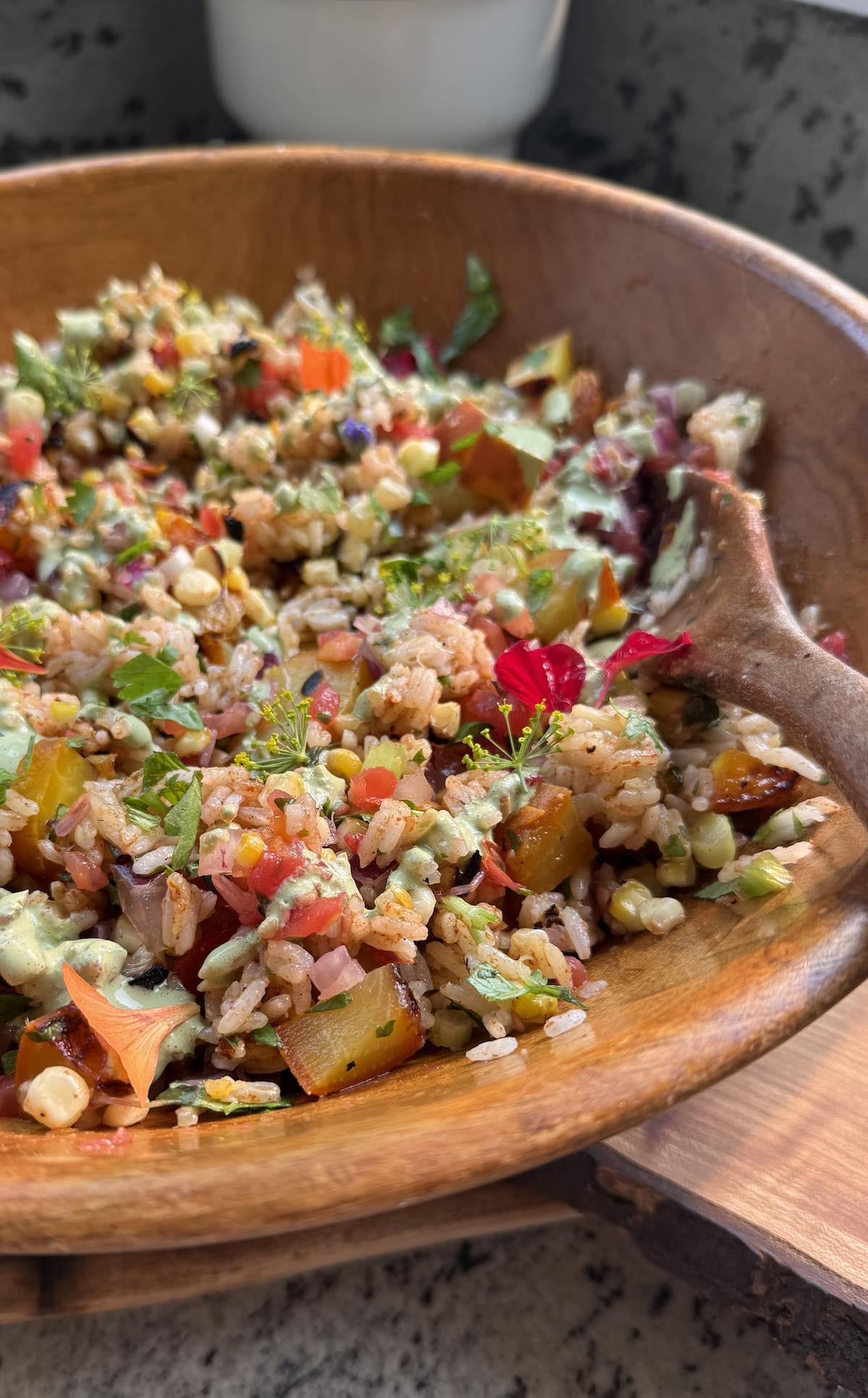 wooden serving bowl of spicy rice salad garnished with edible flowers.