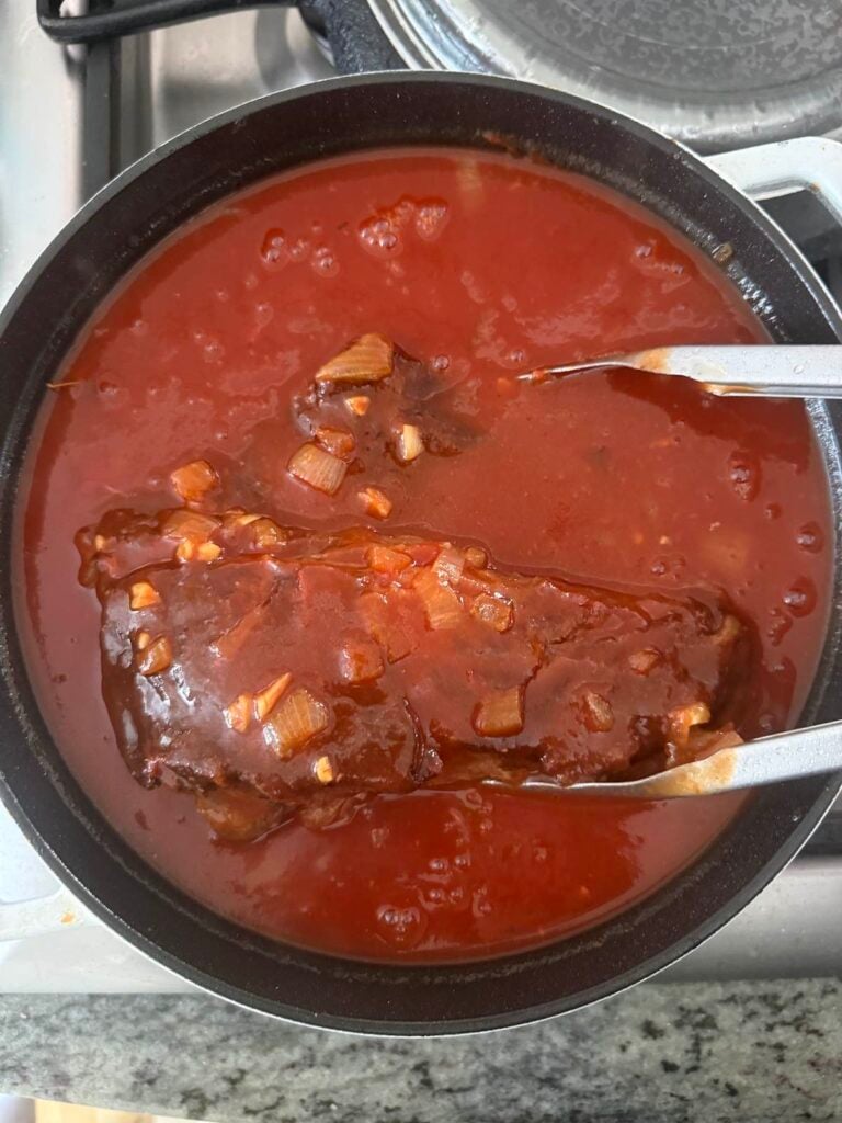 adding seared chuck roast to pot of ragu sauce, to braise in oven.