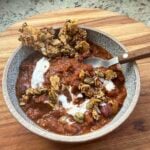 bowl of charred vegetable chili topped with crema, with spoon and tortilla crisps.