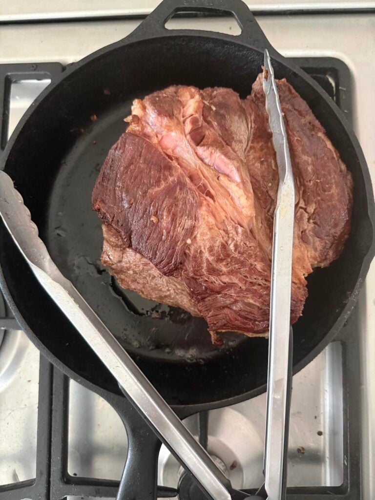 searing a chuck roast in a cast iron skillet.