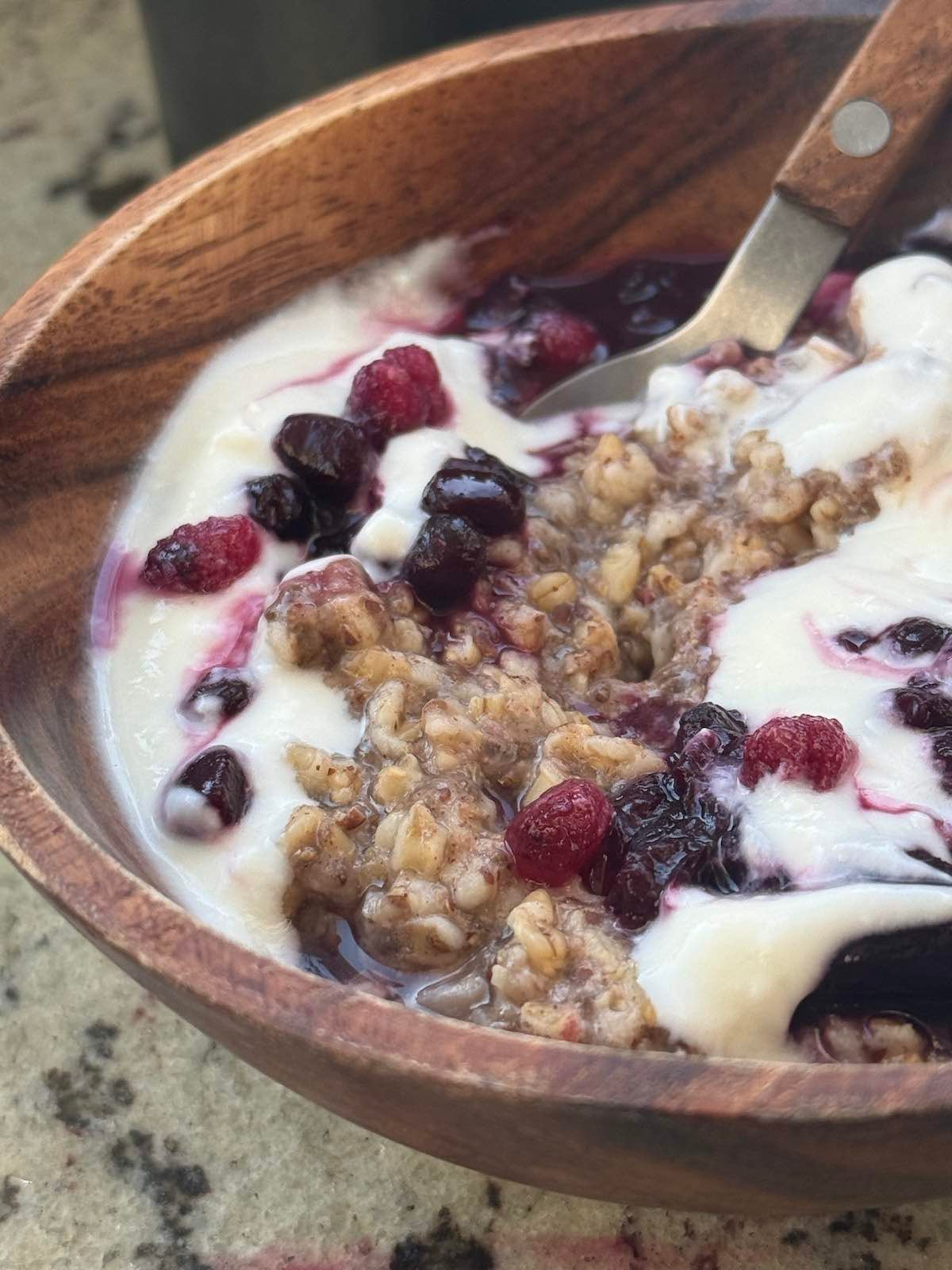 close up of steel cut oats with fruit compote and yogurt in bowl with spoon.