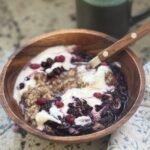 a bowl of steel cut oats topped with yogurt and fruit, and a cup of tea in the background.