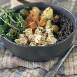 marinated tofu in a bowl with greens, olives, roasted veg and black lentils.