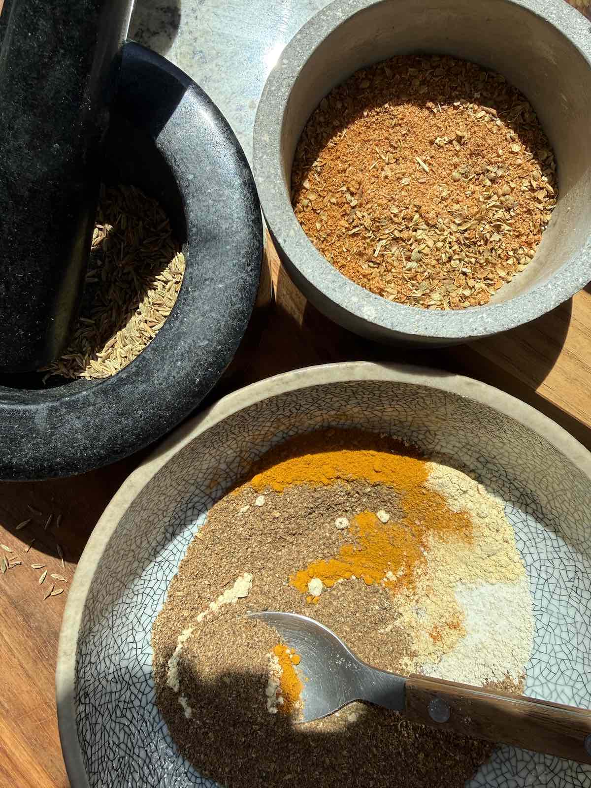 bowls and morter and pestle with whole and ground spices, being mixed together.