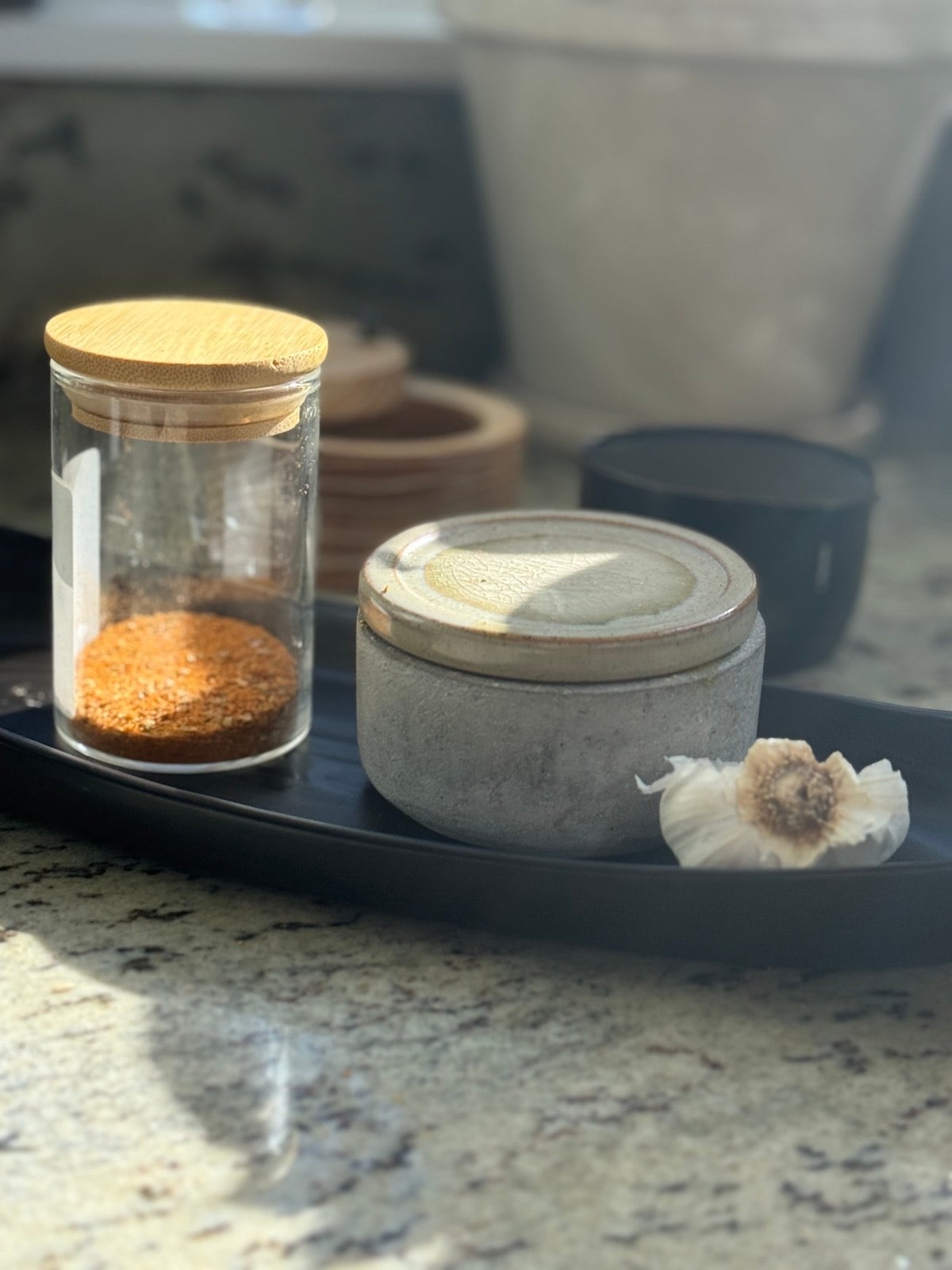 jars and containers of spices and a head of garlic on the kitchen counter.