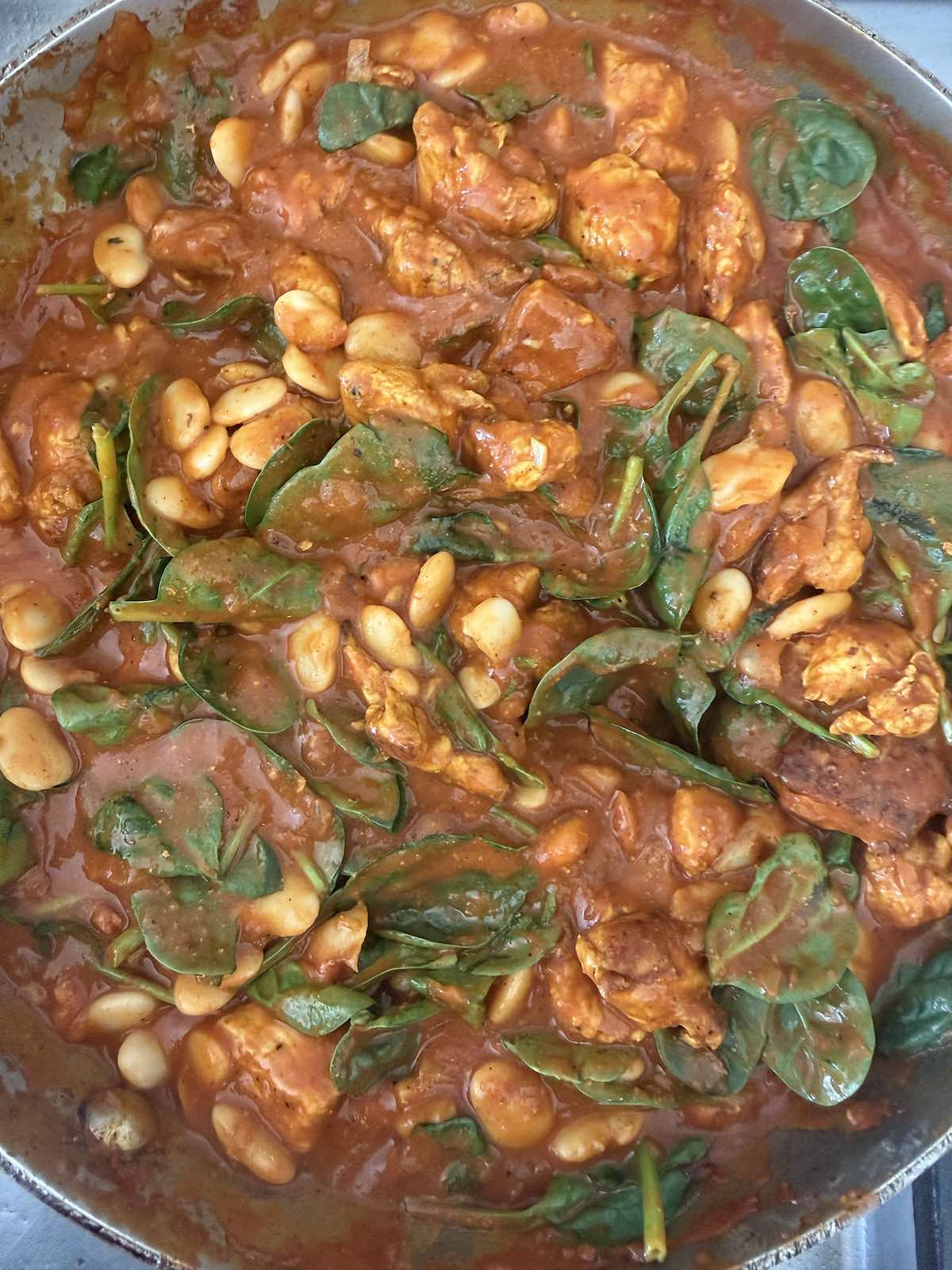 stirring butter beans and spinach into curry sauce.