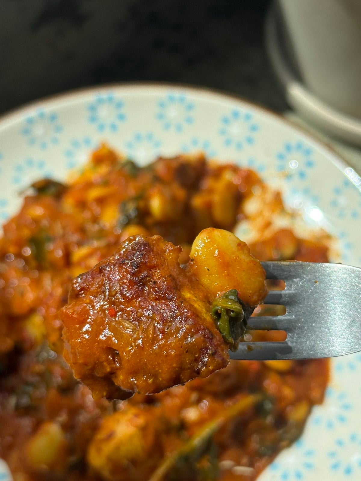 a bite of nicely browned turkey on a fork, held over and above a serving of the turkey curry.