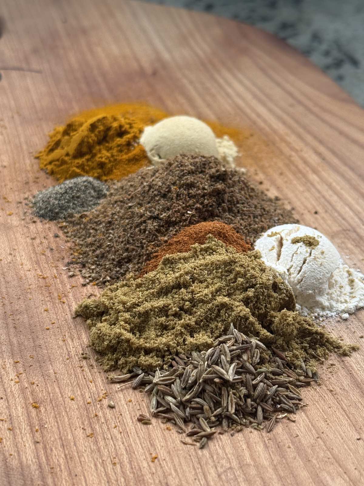 piles of all the spices needed for homemade curry spice mix, laid on a wooden cutting board.