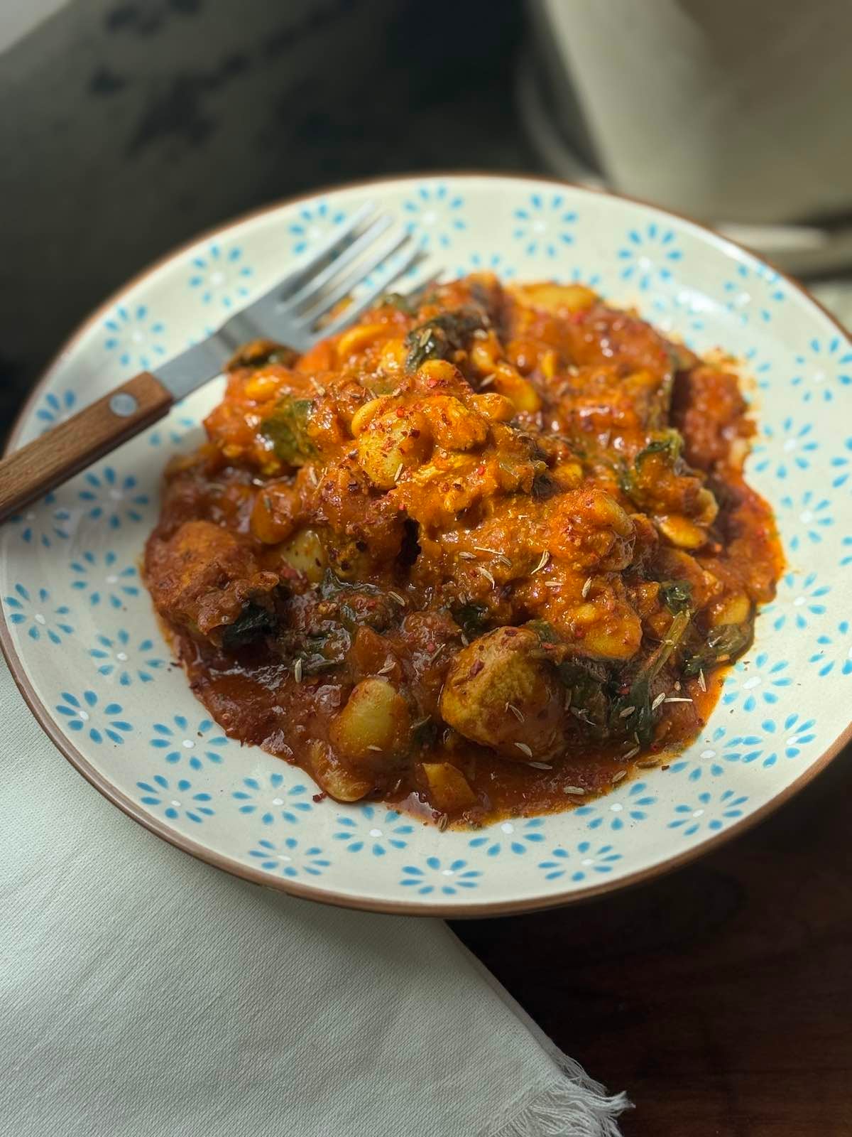 serving of turkey curry in red curry sauce with butter beans and spinach, with napkin and fork.