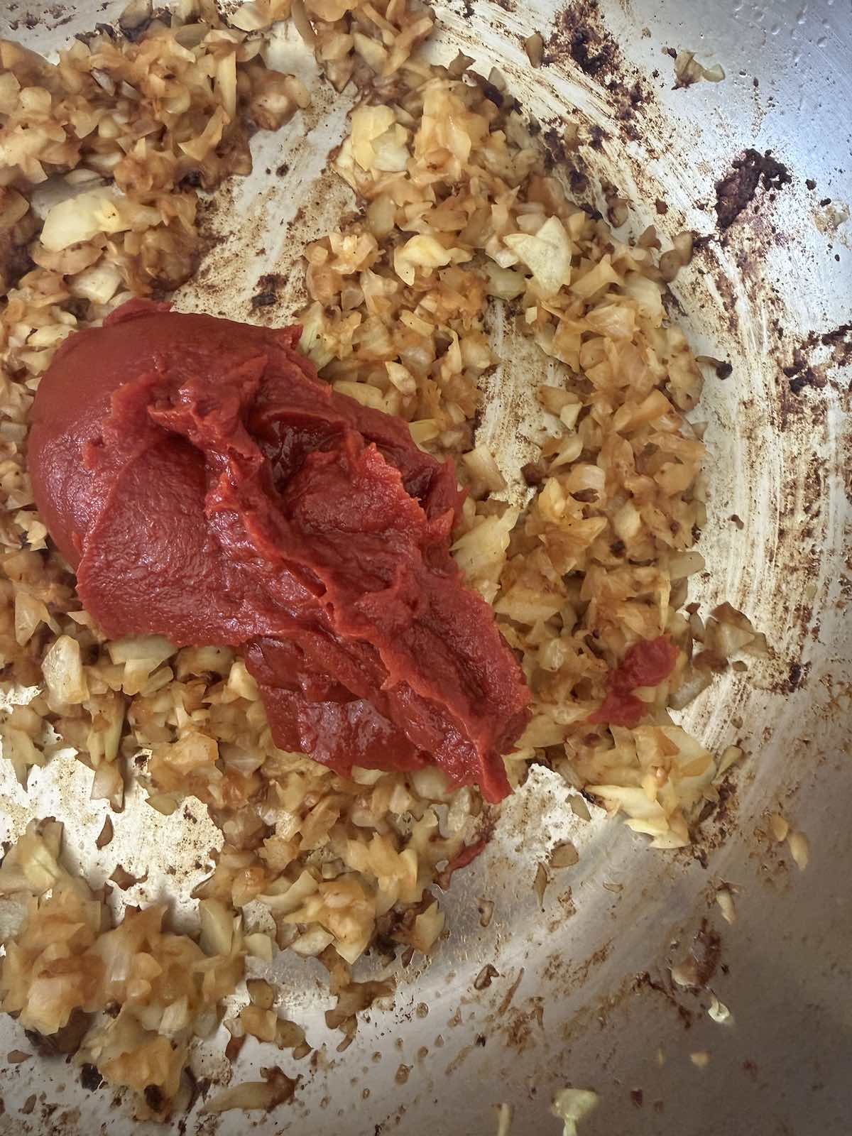 sautéed onions with scoops of tomato paste set on top, ready to be mixed in.