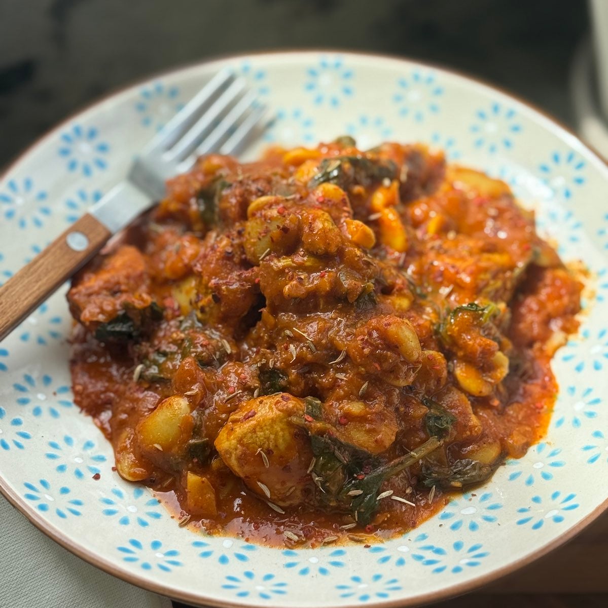 serving of turkey curry in red curry sauce with butter beans and spinach, with napkin and fork.